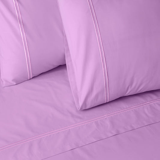 Close-up of orchid colour luxury embroidered bedding with two pillows on a matching bed sheet.