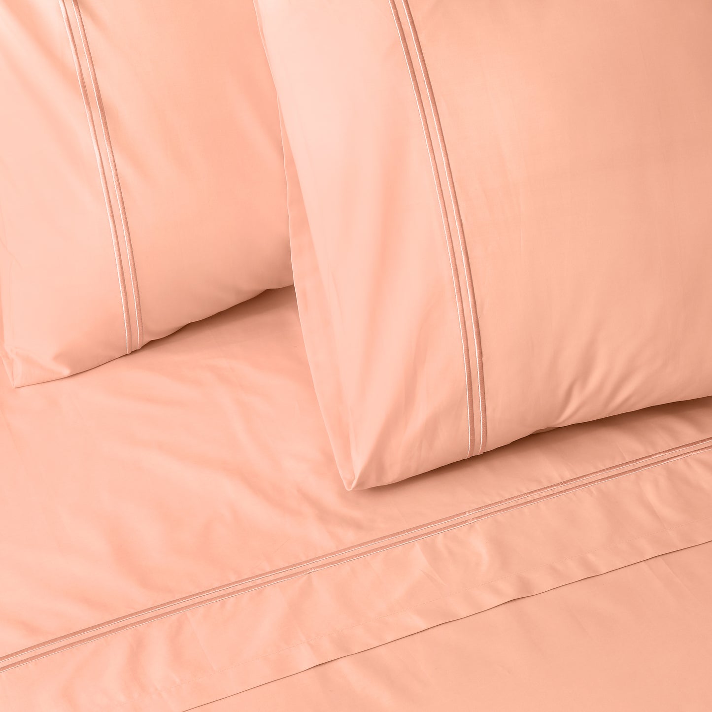 Close-up of peach colour luxury embroidered bedding with two pillows on a matching bed sheet.