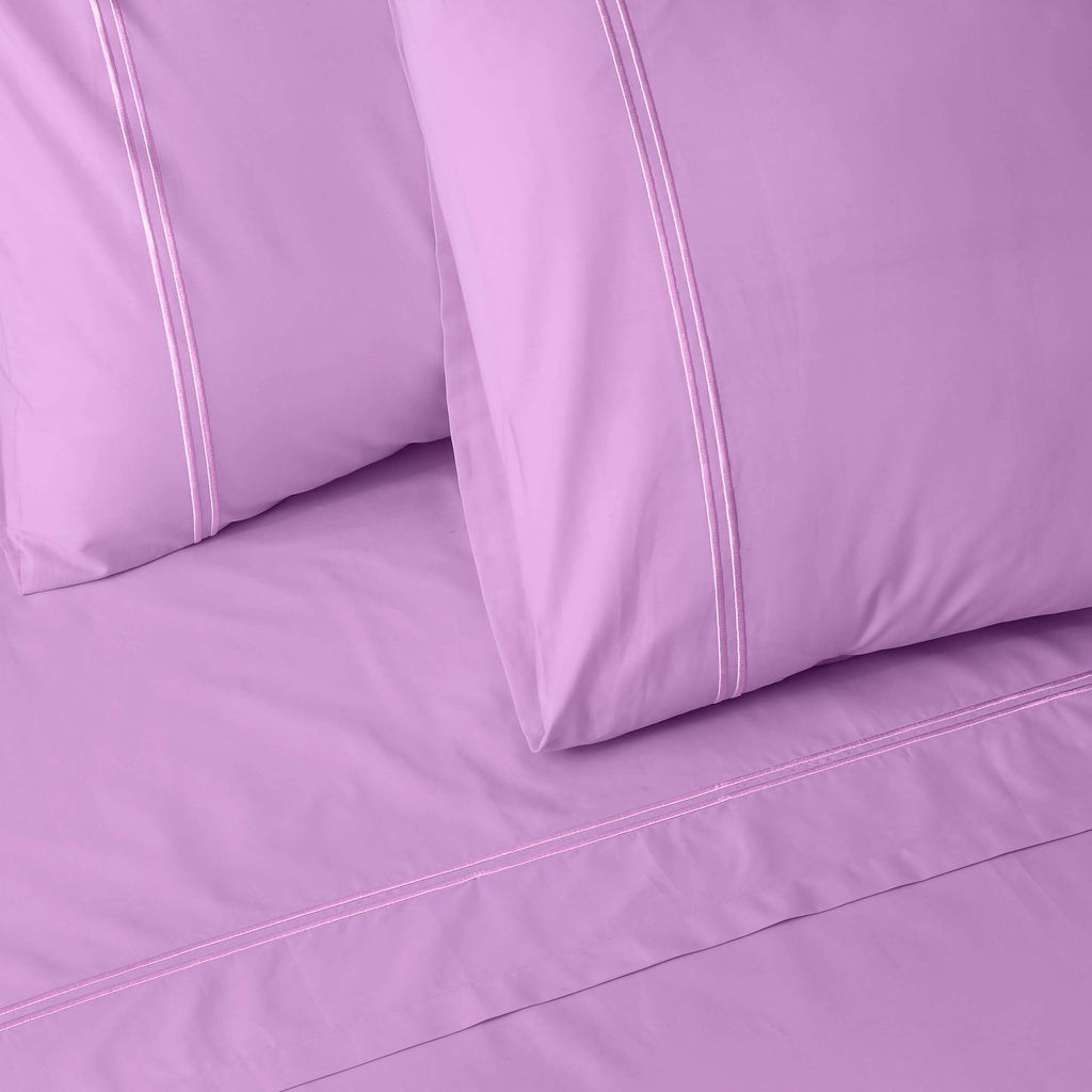 Close-up of orchid colour luxury embroidered organic cotton bedding with two pillows on a matching bed sheet.