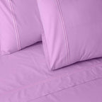 Close-up of orchid colour luxury embroidered organic cotton bedding with two pillows on a matching bed sheet.