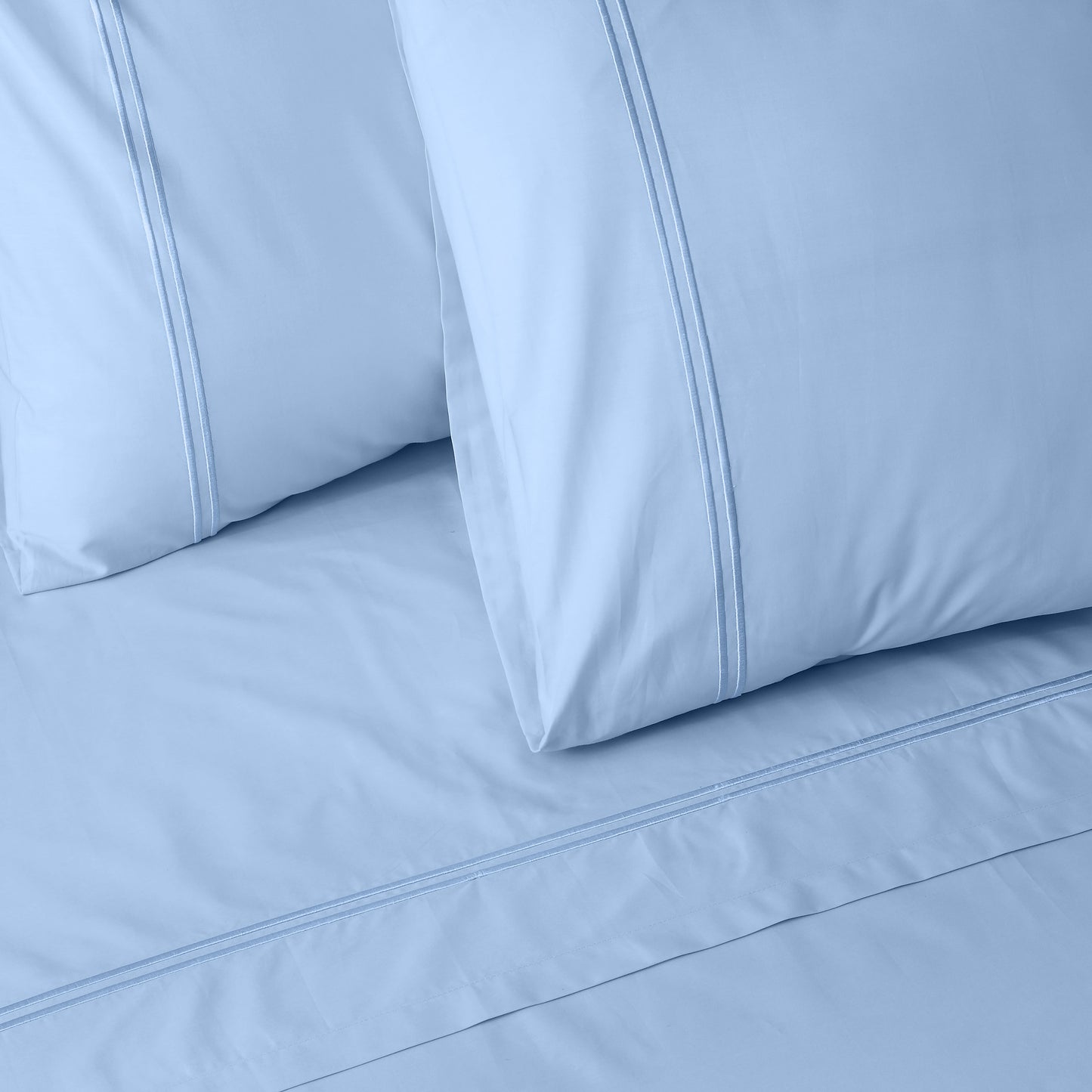 Close-up of mirage colour luxury embroidered bedding with two pillows on a matching bed sheet.