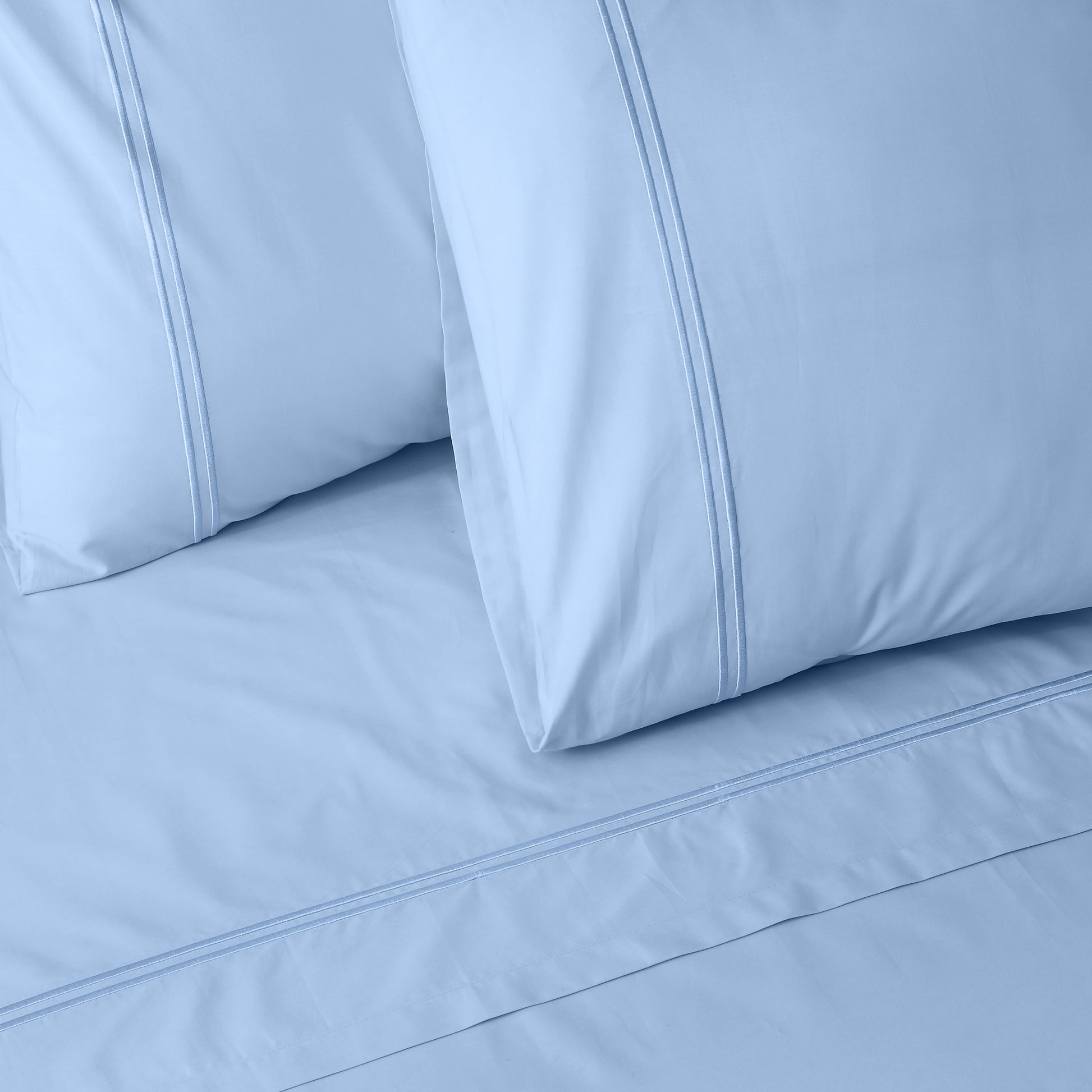 Close-up of mirage colour luxury embroidered bedding with two pillows on a matching bed sheet.