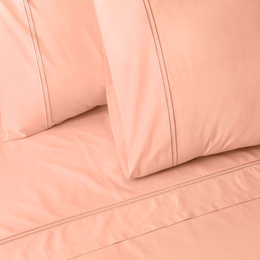 Close-up of peach colour luxury embroidered organic cotton bedding with two pillows on a matching bed sheet.
