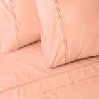 Close-up of peach colour luxury embroidered organic cotton bedding with two pillows on a matching bed sheet.