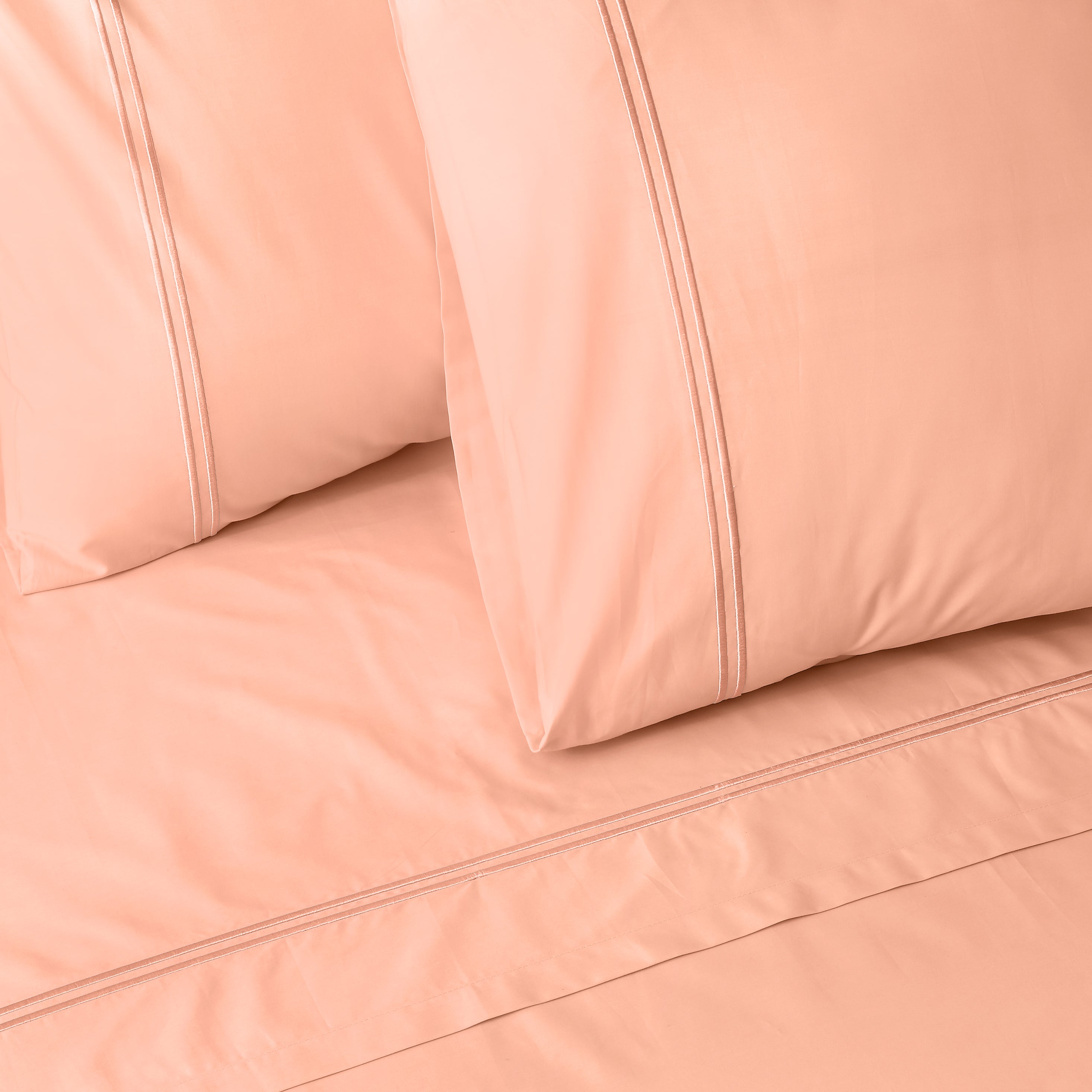 Close-up of peach colour luxury embroidered bedding with two pillows on a matching bed sheet.
