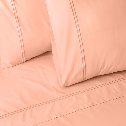 Close-up of peach colour luxury embroidered bedding with two pillows on a matching bed sheet.