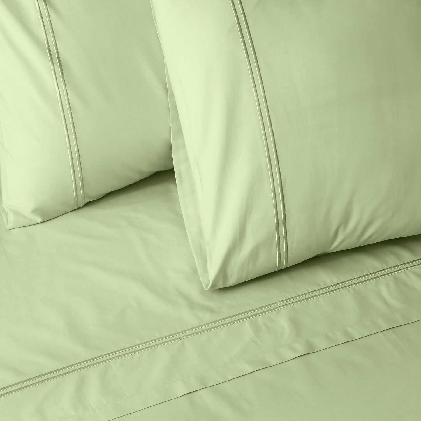 Close-up of light green colour luxury embroidered bedding with two pillows on a matching bed sheet.