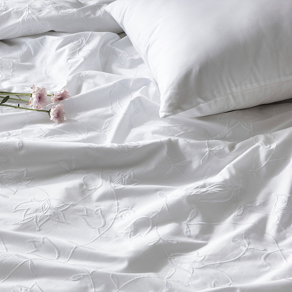 White bedding set with floral embroidery and a pillow on a plain background
