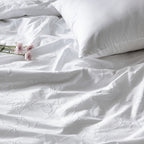 White bedding set with floral embroidery and a pillow on a plain background