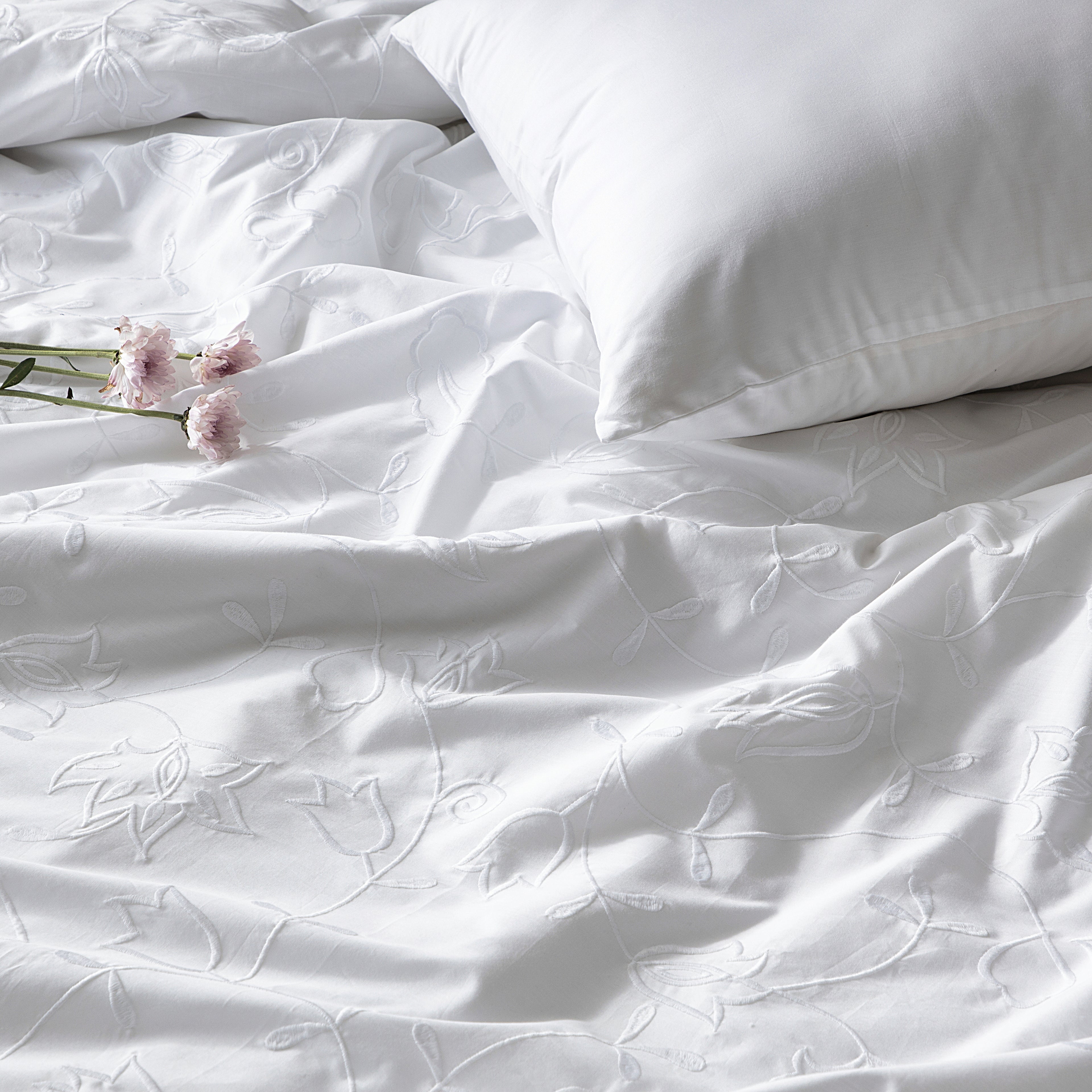 White bedding set with floral embroidery and a pillow on a plain background