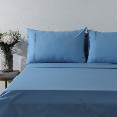 Blue Mirage dyed organic cotton sheet set on a styled bed – soft blue flat sheet and pillowcases with minimalistic embroidery, 200 TC organic cotton percale, Whites of London India