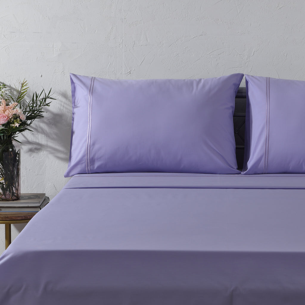 Lavender Mist dyed organic cotton sheet set on a styled bed – soft pastel lavender flat sheet and pillowcases with minimalistic embroidery, 200 TC percale, Whites of London India