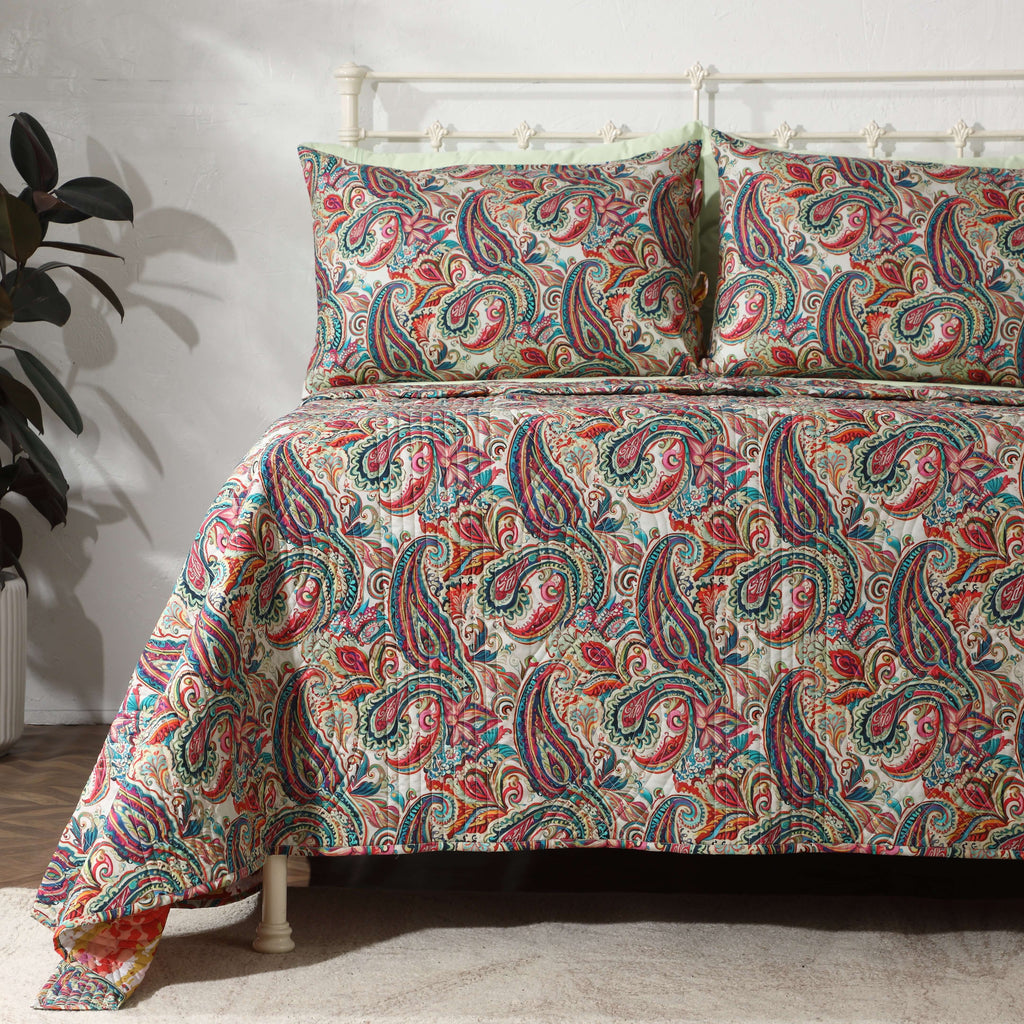 Paisley Romance quilted dohar set on a made bed – intricate paisley motifs in rich teal and coral tones, lightly quilted organic cotton percale