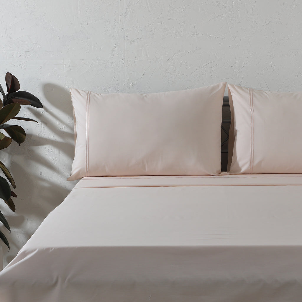 Peach Mist dyed organic cotton sheet set on a styled bed – soft pastel peach flat sheet and pillowcases with minimalistic embroidery, 200 TC, Whites of London India