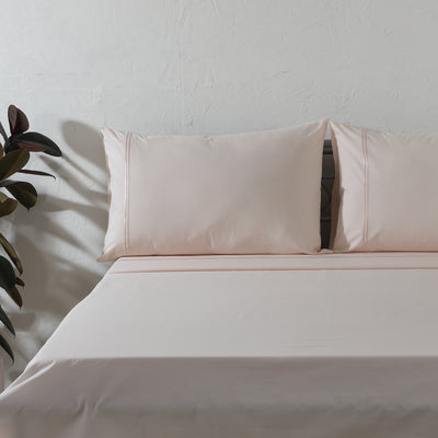 Peach Mist dyed organic cotton sheet set on a styled bed – soft pastel peach flat sheet and pillowcases with minimalistic embroidery, 200 TC, Whites of London India