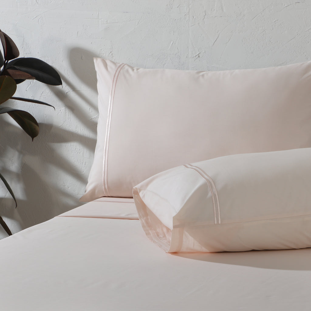 200TC dyed organic cotton sheet set in Peach Mist on a made bed – soft pastel tone, minimalistic embroidery, breathable and gentle on the skin, Whites of London