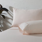 200TC dyed organic cotton sheet set in Peach Mist on a made bed – soft pastel tone, minimalistic embroidery, breathable and gentle on the skin, Whites of London