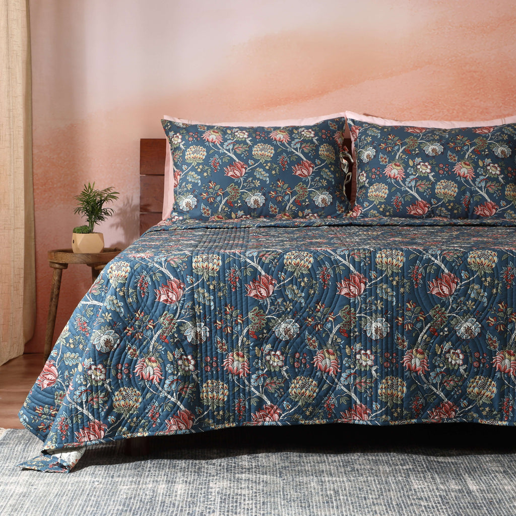 Quilted Chintz dohar draped on a bed – rich deep blue base with delicate floral and vine print, reversible organic cotton percale, Whites of London India