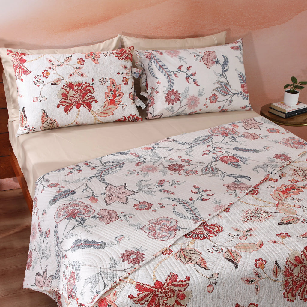 Ivory side of the Jacobean Summer percale dohar on a bed – soft blush-coral and slate-blue cotton percale botanical print, reversible with wave-quilted texture