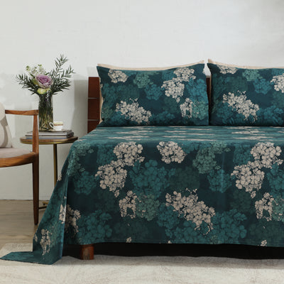 Hydrangea organic cotton percale sheet set on a styled bed – cascading blooms in blue, violet and white on a deep moody teal ground, 200 TC GOTS-certified, Whites of London India