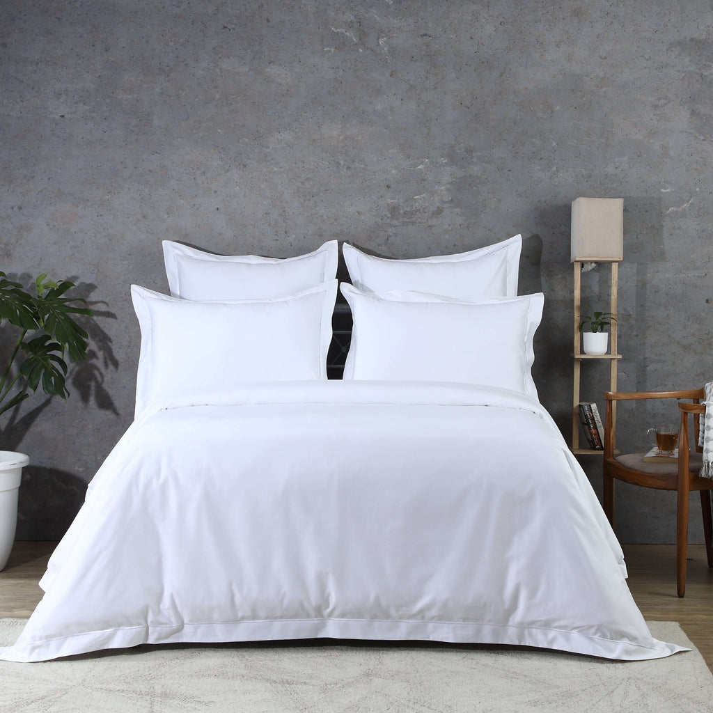 White organic cotton bedding set on a bed against a grey wall with a plant and small table in the background.